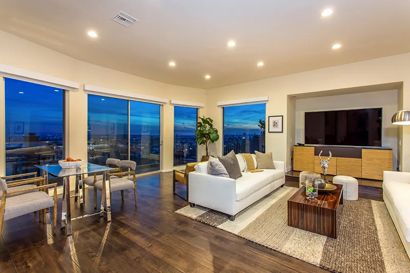 Single-story house with a terracotta-tiled roof, archway entrance, plants in the yard, and a paved driveway. Bright, sunny day, tropical vibe.