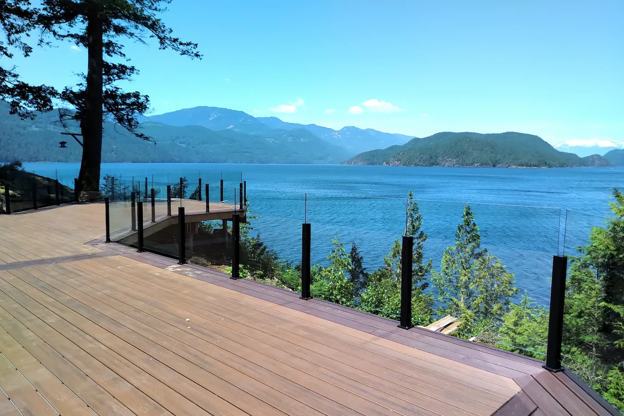 Semi-frameless glass railings with slim aluminum posts on a cedar deck overlooking water and mountains in British Columbia.