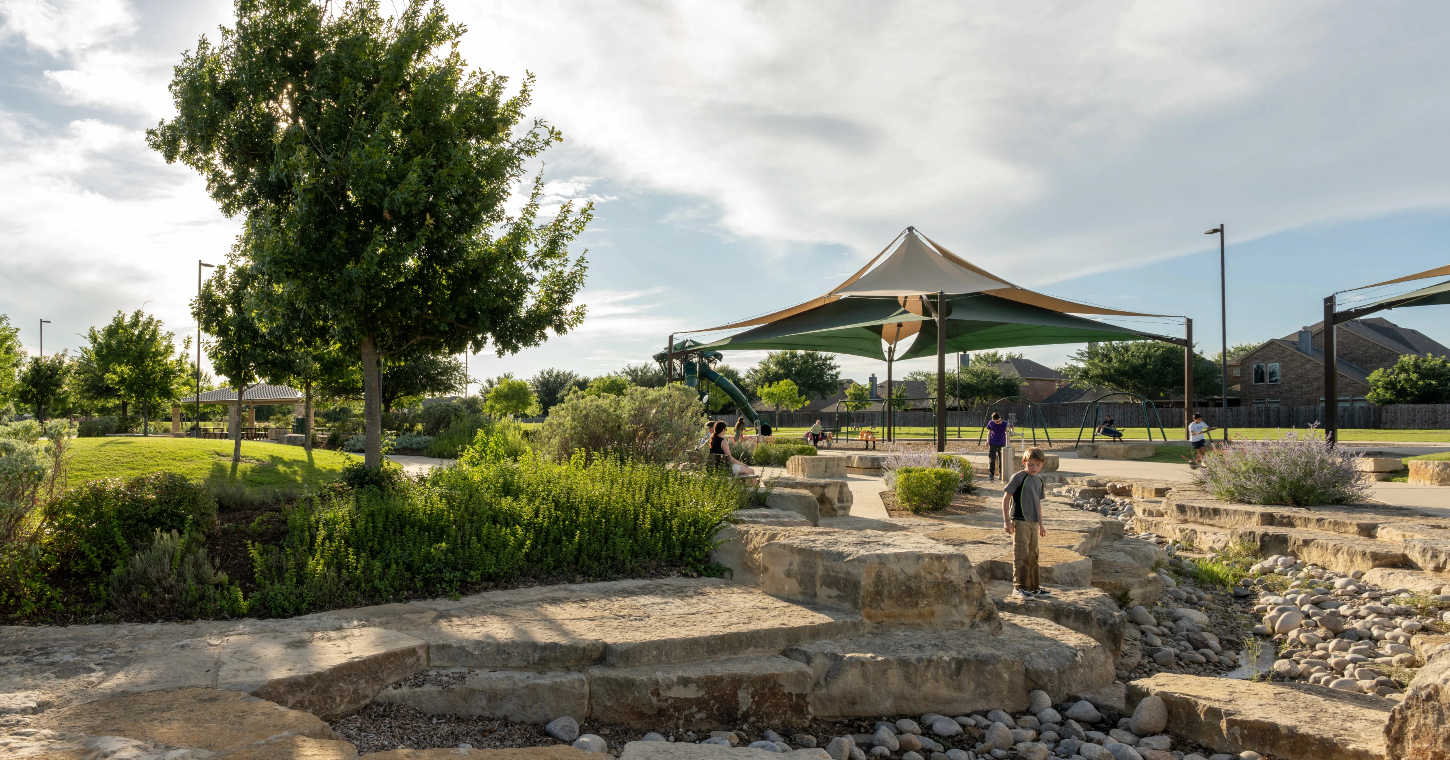 Landscape architecture park with native plantings, stone terracing, and tensile shade structures in North Texas