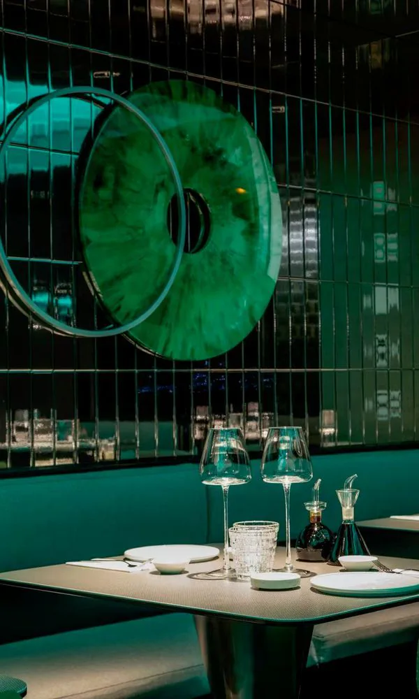 Grand disque vert jade cerclé de chrome devant un mur de carreaux verts, au-dessus d’une banquette
