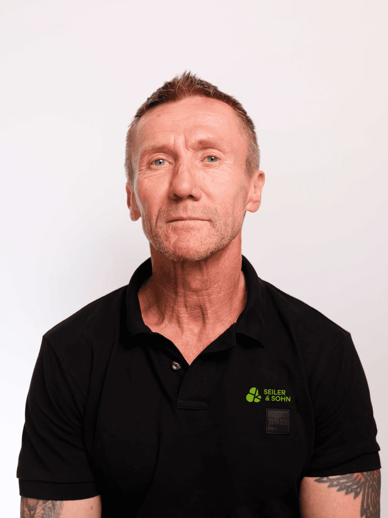Nahaufnahme des schwarzen Polo-Shirts eines Mitarbeiters mit dem Seiler & Sohn Logo auf der Brust – Kleeblatt-Icon in Grün mit Schriftzug.