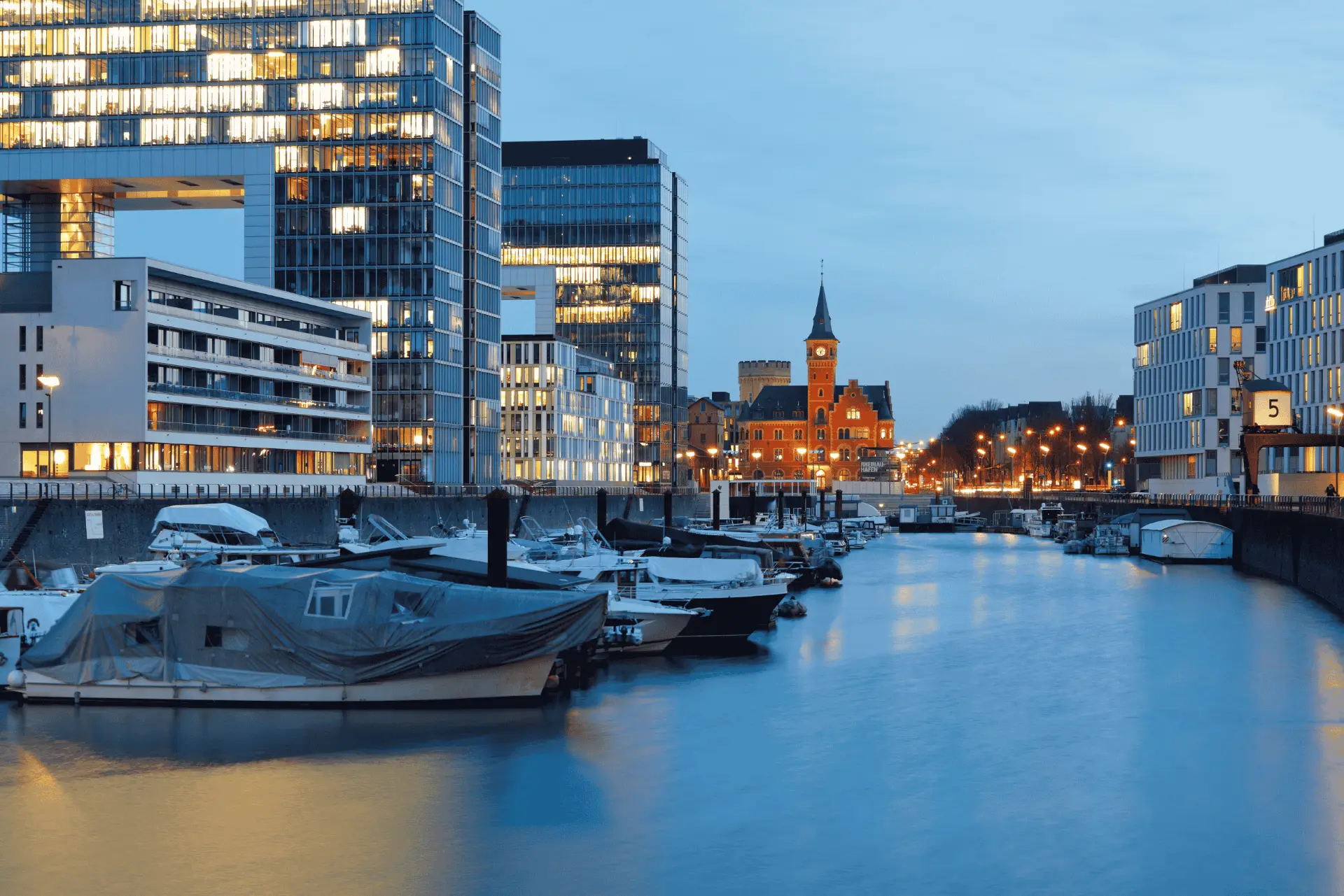 Eine ruhige Kanalszene in der Dämmerung mit festgemachten Booten, die moderne Gebäude und historische Architektur widerspiegeln.