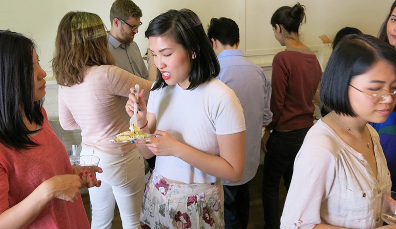 snapshot of people in a class having cake and beverages