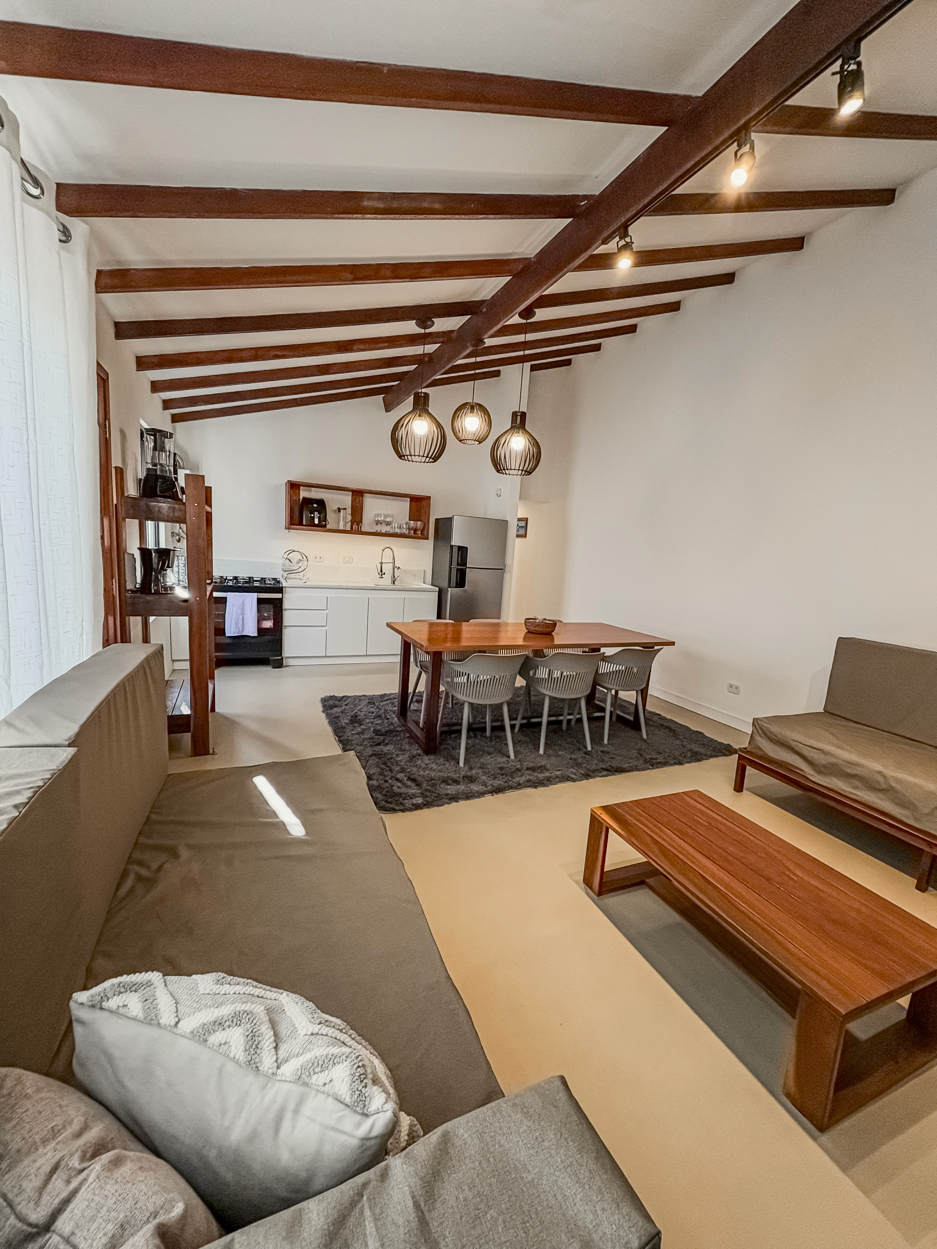 A stylish split-level loft room with an elevated queen bed, modern writing desk below, and floor-to-ceiling windows framing a glowing sunset.