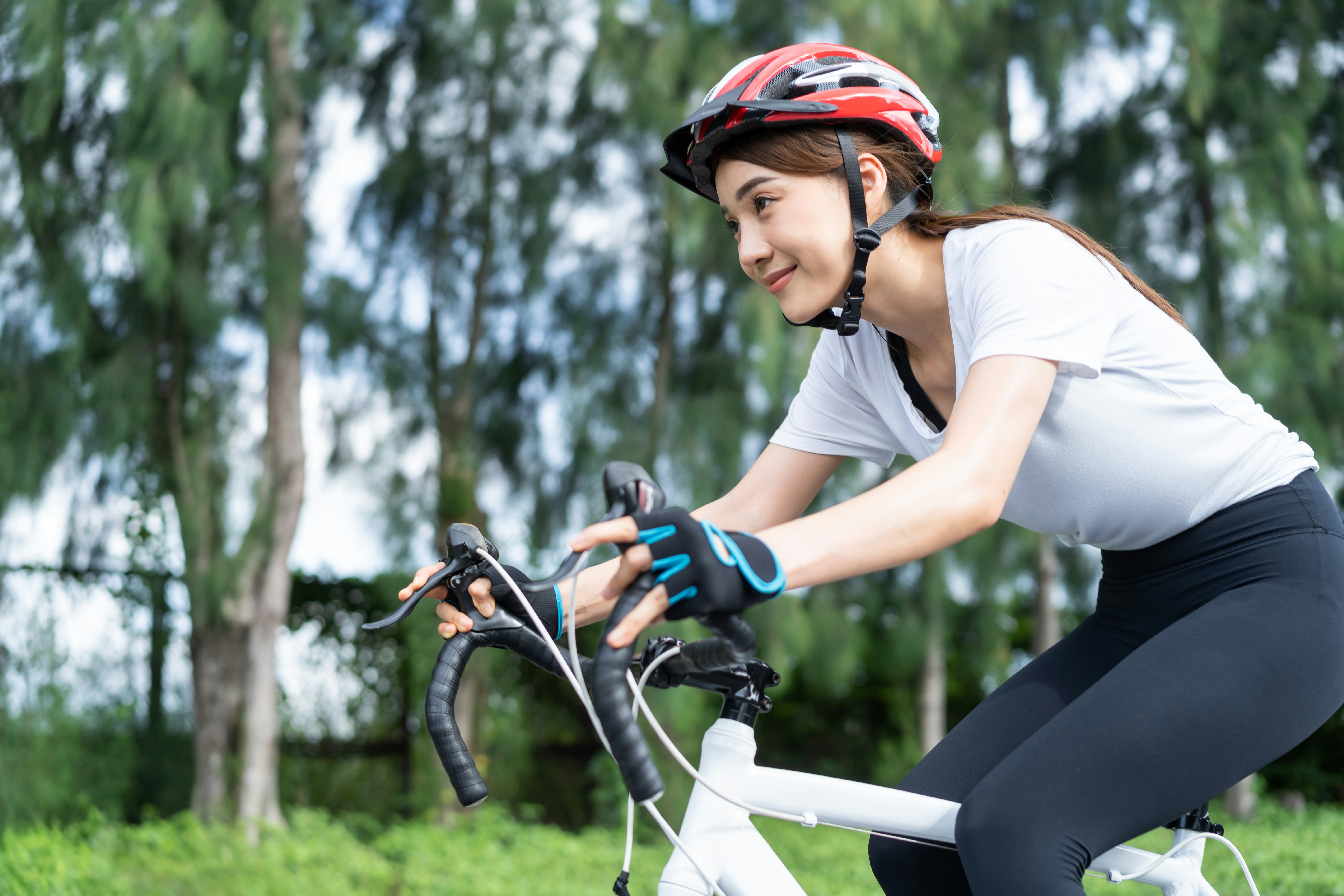 A person wearing a helmet rides a bicycle through a lush green area, smiling as they pedal.