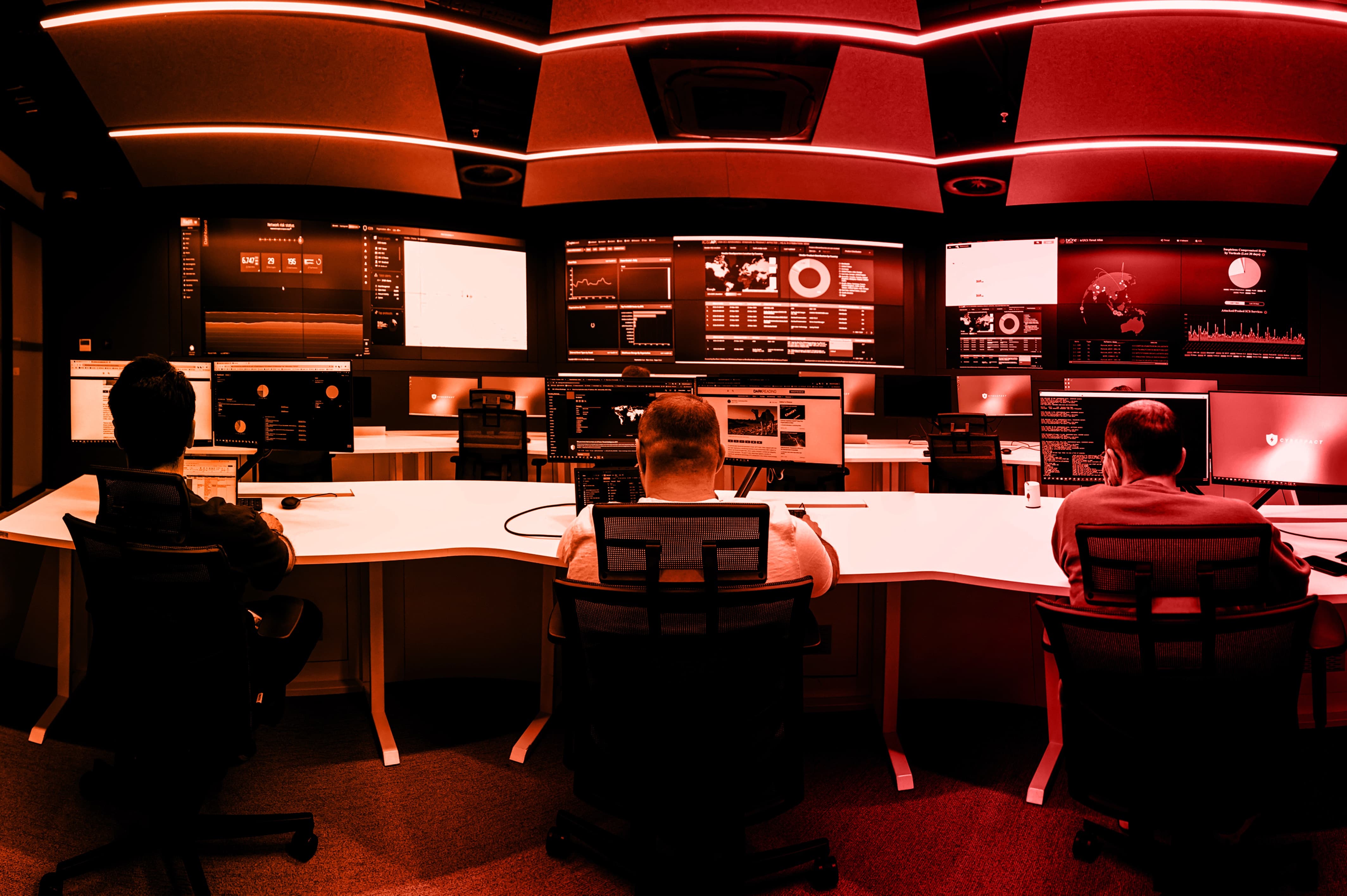 A person sits in front of multiple screens in a dimly lit control room, focused on the displays.