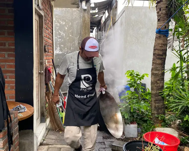 Dedicated head chef carries a large wok through the outdoor kitchen during a community meal program