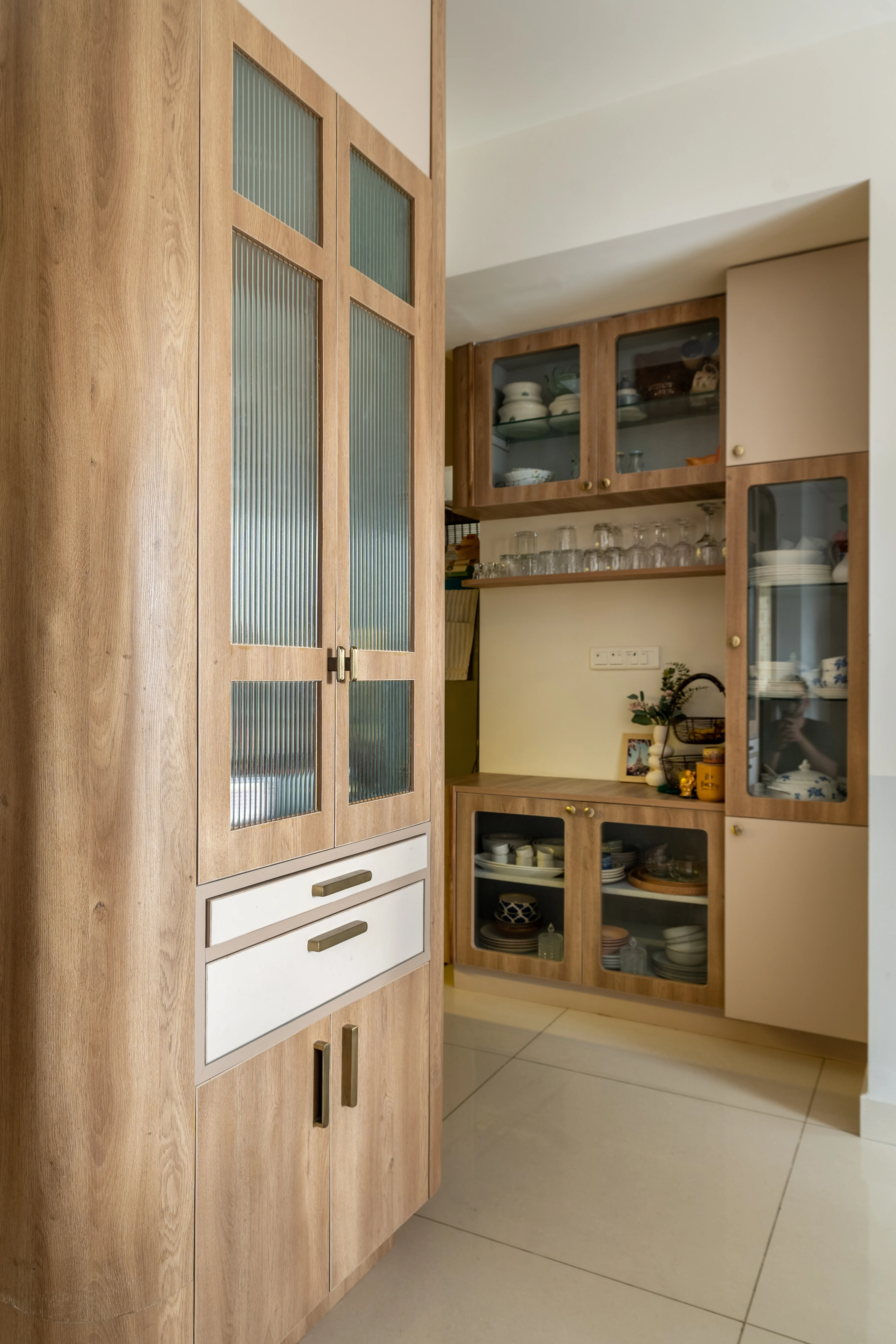 A kitchen featuring a wooden cabinet with glass doors on the left, and a display cabinet with open shelves on the right. The display cabinet holds various dishes and glassware.