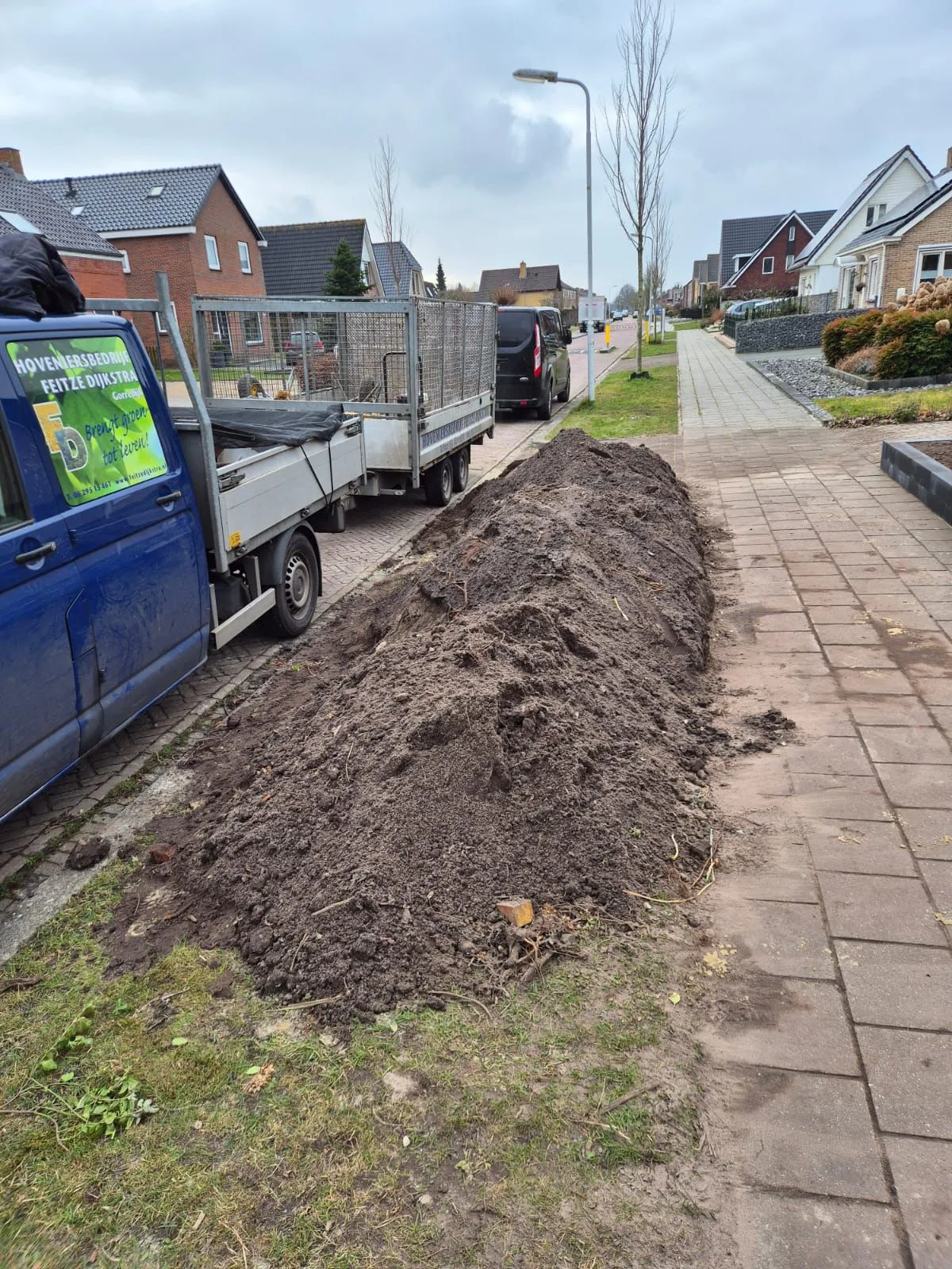 Voortuin in Harkema in renovatiefase met afgegraven grond langs stoep en geparkeerde bus van hoveniersbedrijf Feitze Dijkstra.