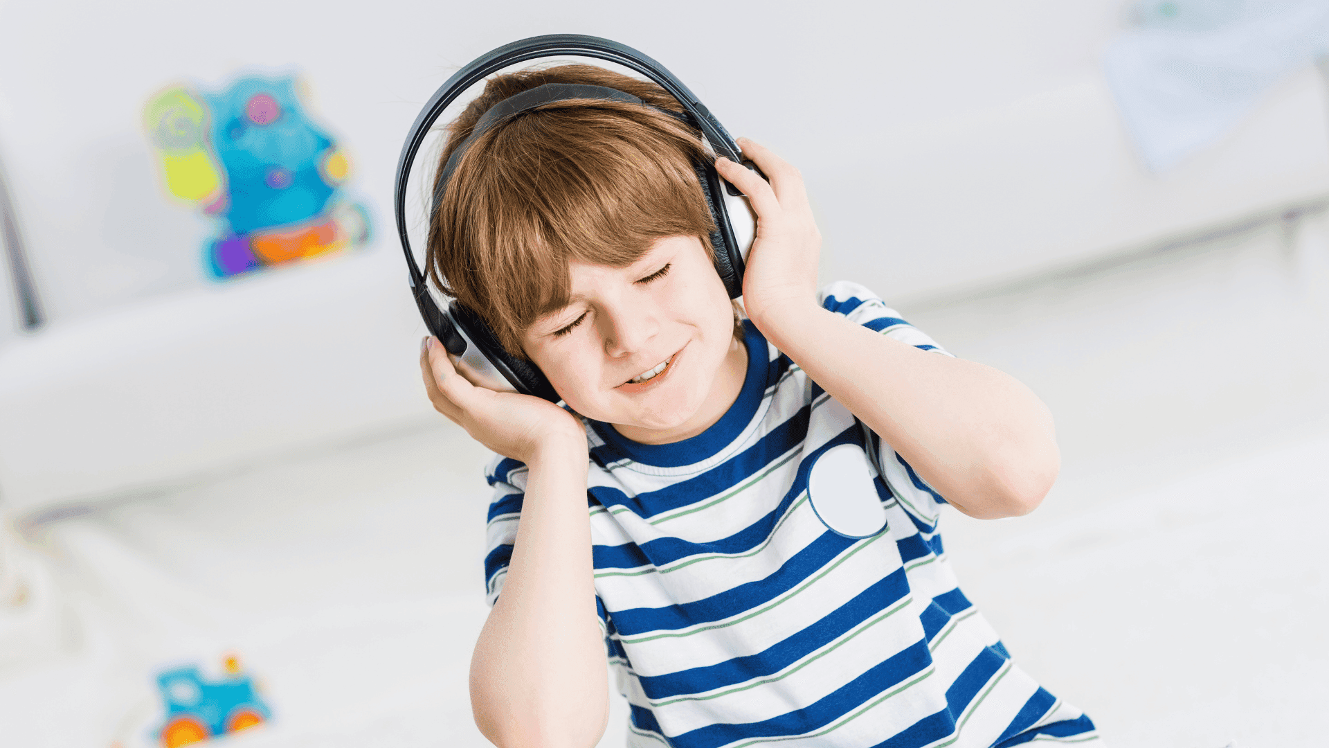 A boy wearing a striped blue t shirt and headphones, smiling and looking happy.