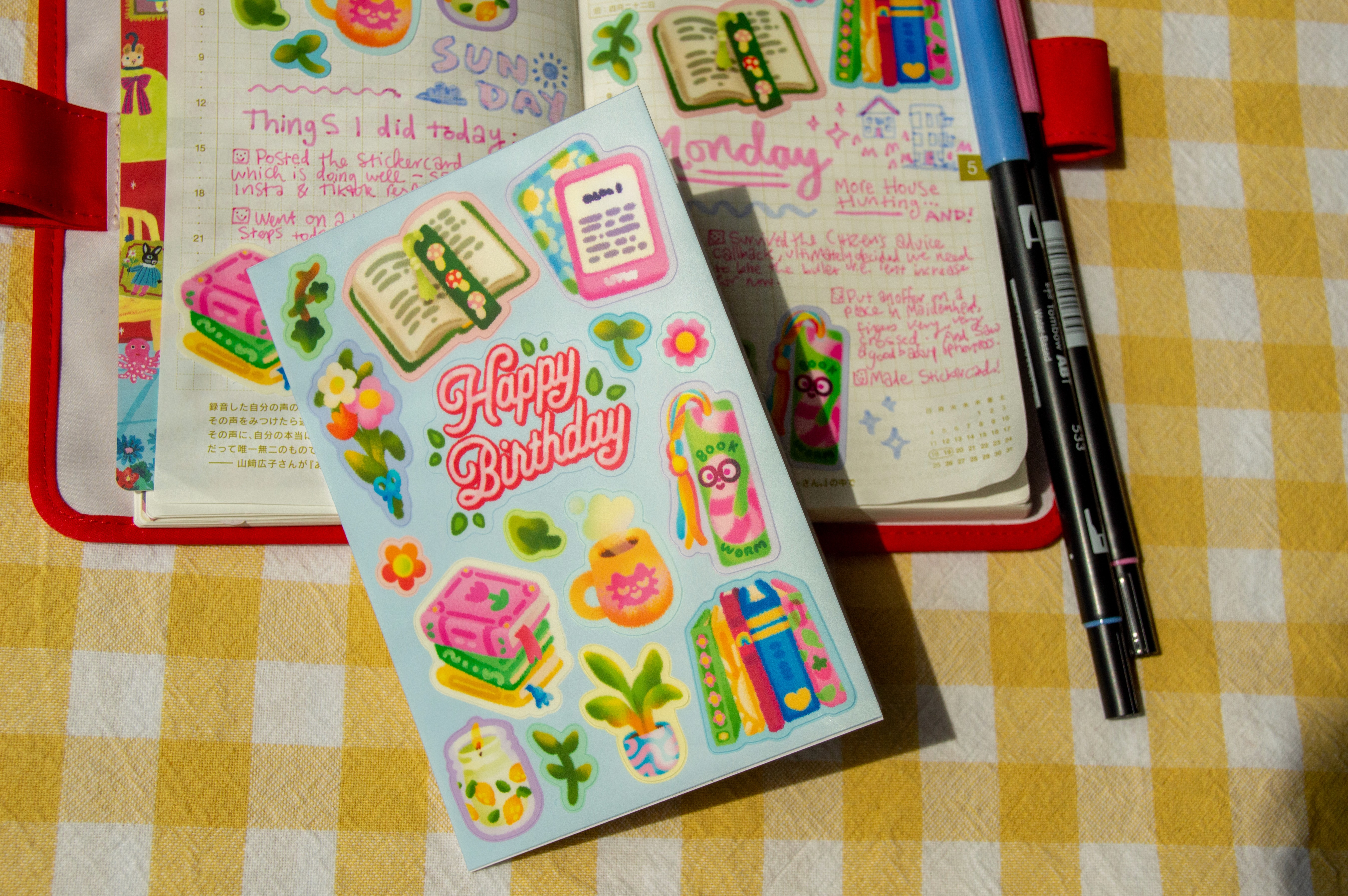 A book-themed stickercard rests on top of a diary spread that uses some of the stickers in the design on the page.