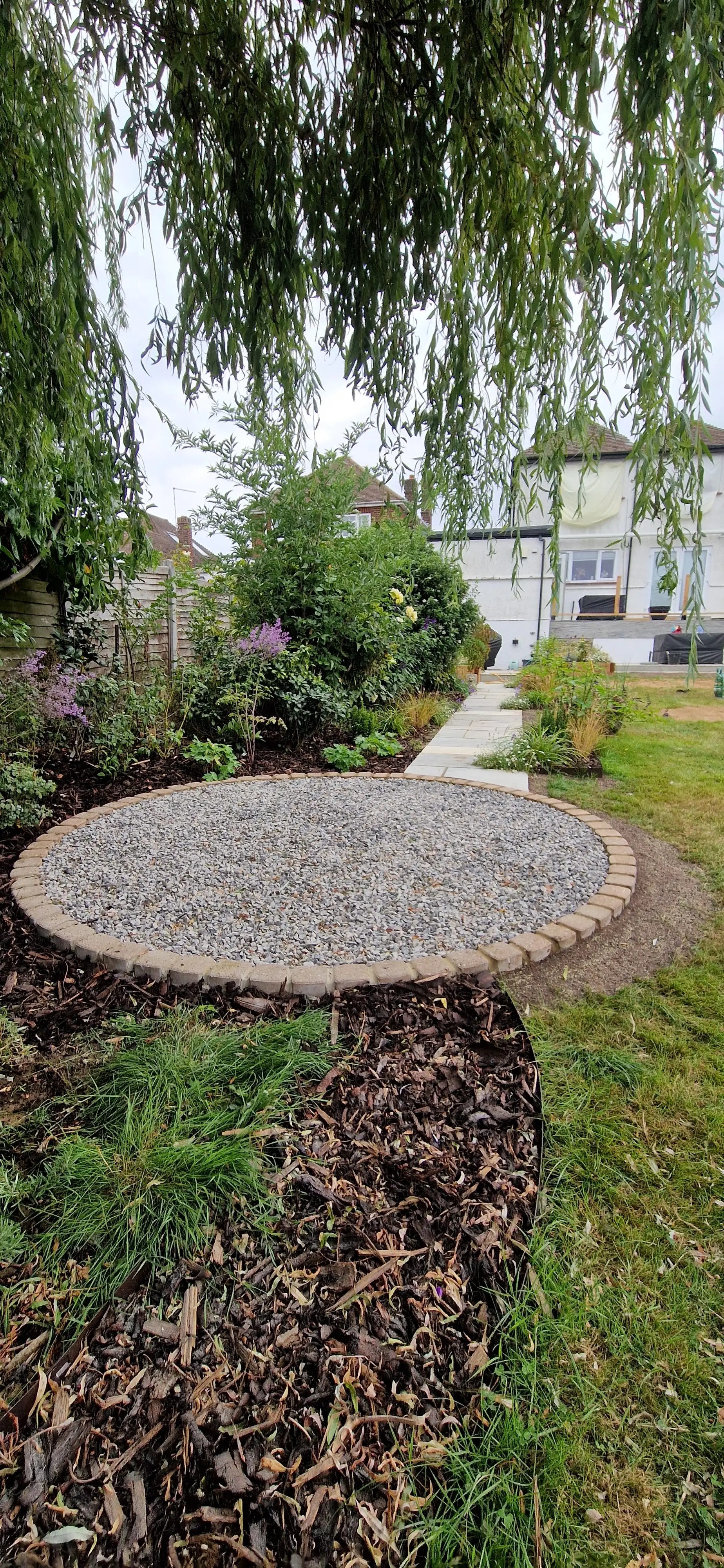 A round stone table surrounded by greenery, with a pathway leading away in the background.