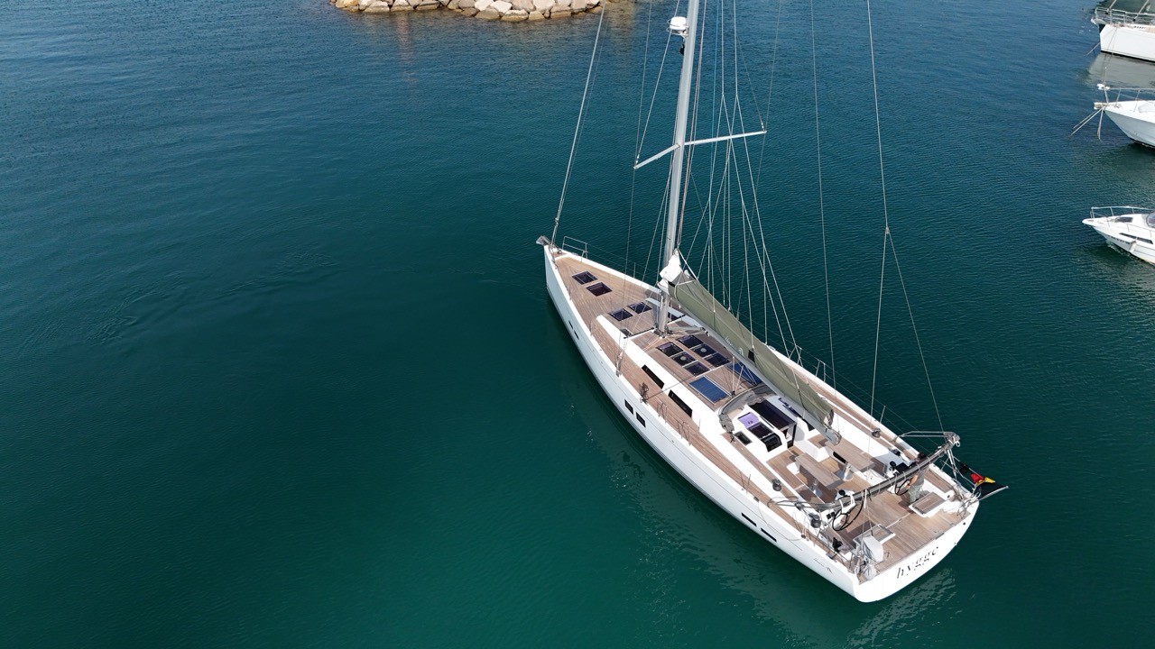 Beneteau Clipper 361 sailing yacht motoring at anchor in calm blue waters off Valletta, Malta, showing the full port profile with white hull, furled mainsail, bimini with solar panel, B&G instruments on the stern arch, and the iconic Valletta skyline with St Paul's Cathedral dome and historic limestone fortifications behind