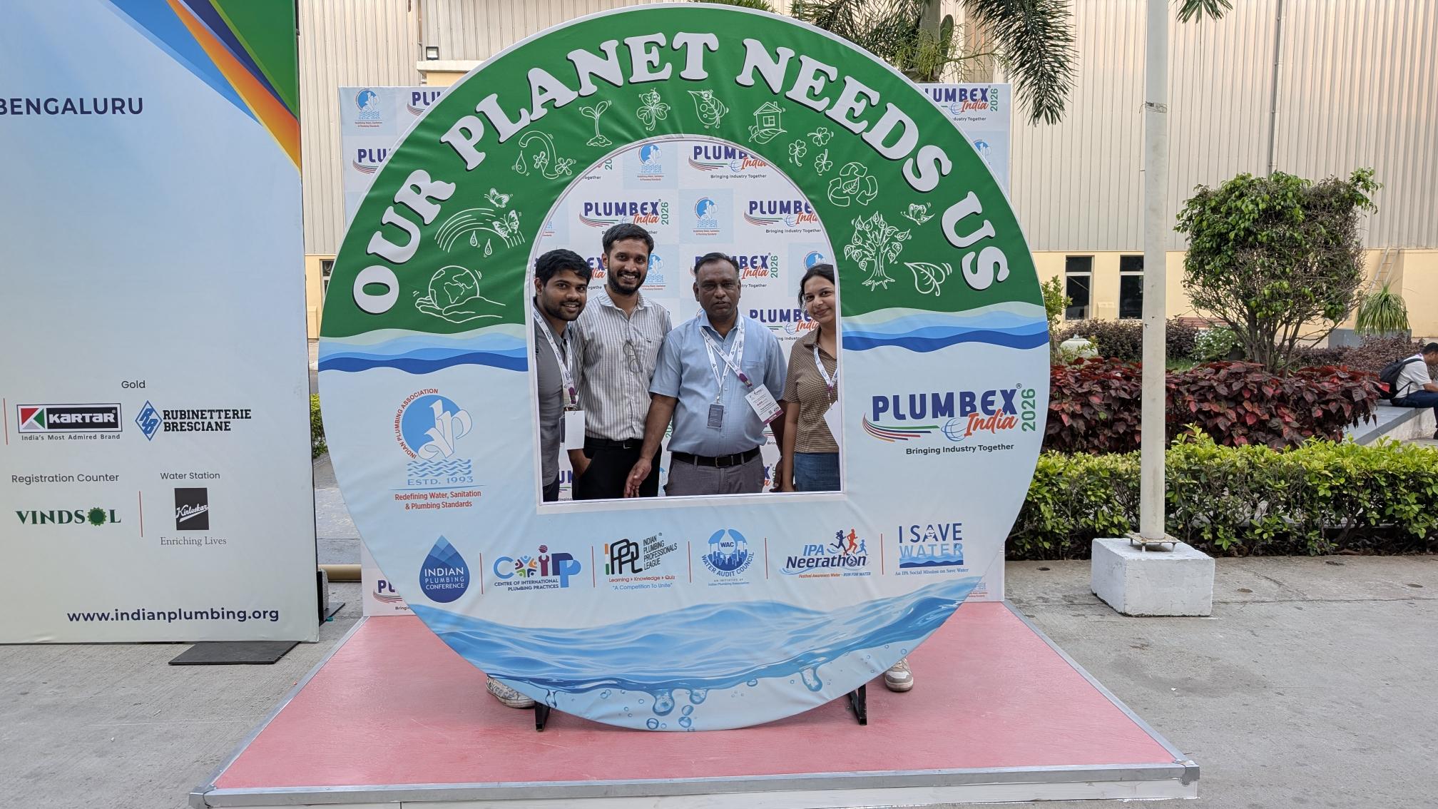 A man stands while two people sit at a table in an office setting, smiling and engaged in conversation. The mood is friendly and collaborative.