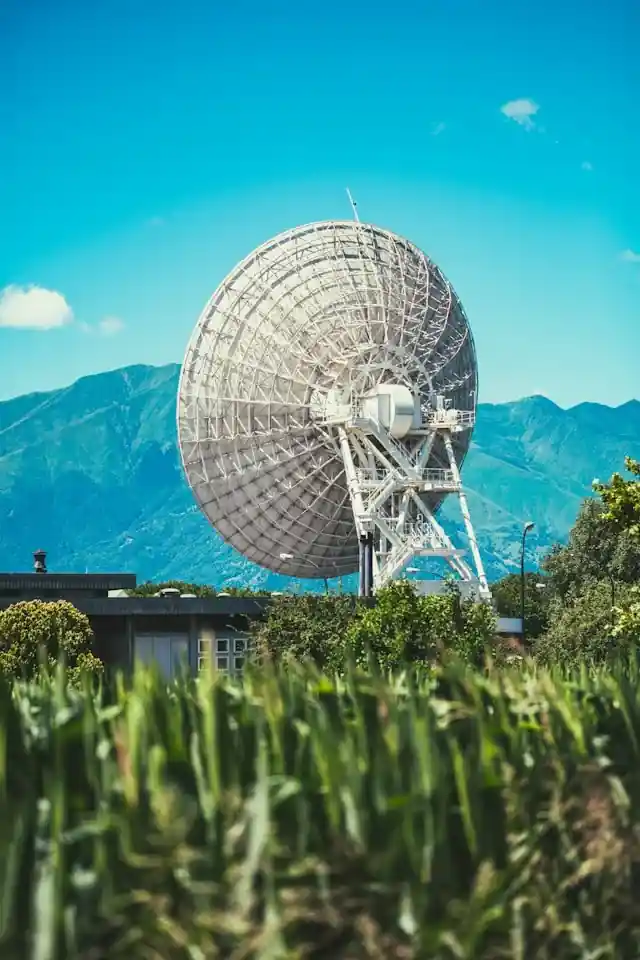 Large satellite dish in a field with mountains behind it