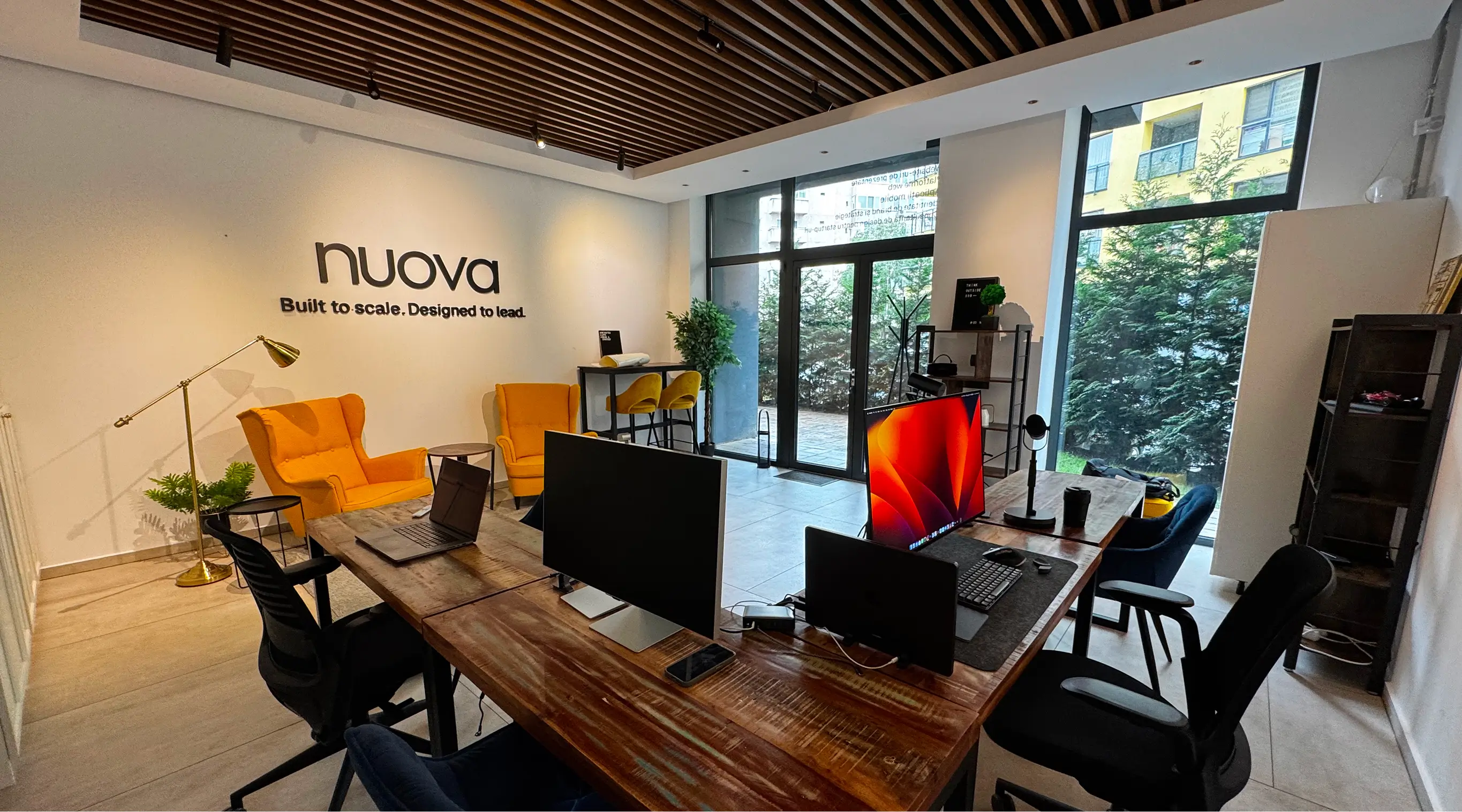 A modern office with colourful furniture, with working stations and big windows showing pine trees