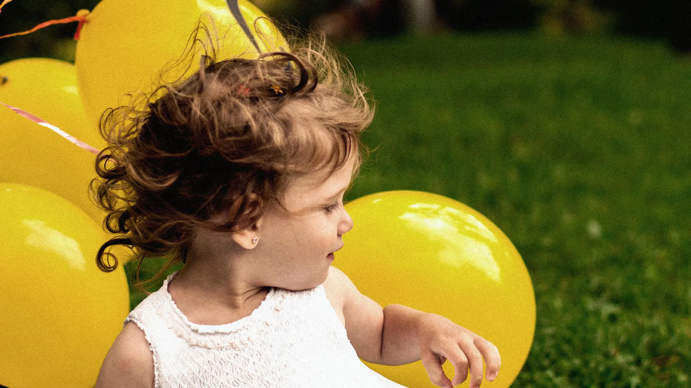 A child holding bright yellow balloons in a green public park setting.