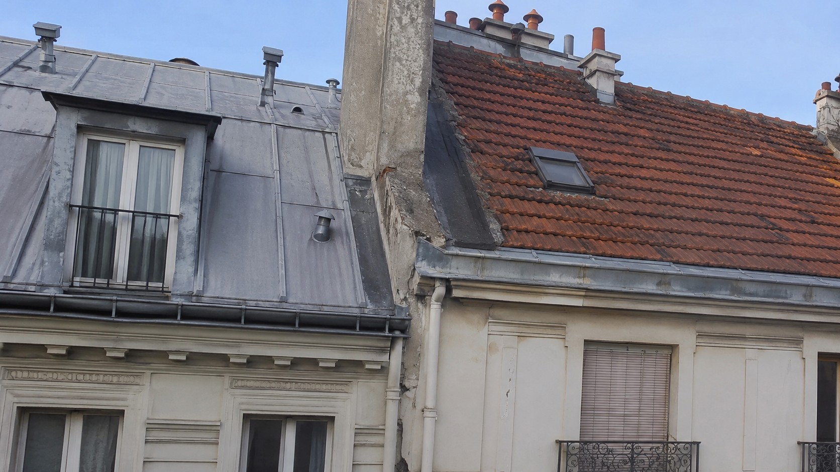 Photo réaliste d’une toiture mitoyenne en copropriété à Paris, montrant la jonction entre deux immeubles avec une toiture en zinc, une toiture en tuiles rouges, un mur séparatif, des solins, gouttières et cheminées, illustrant la répartition des réparations entre deux bâtiments voisins.