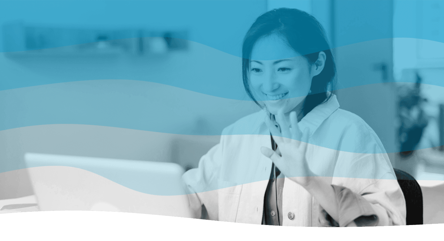 A modern workspace features a sleek computer displaying a video call with a person, surrounded by neatly arranged office supplies, plants, and a steaming mug on a wooden desk.