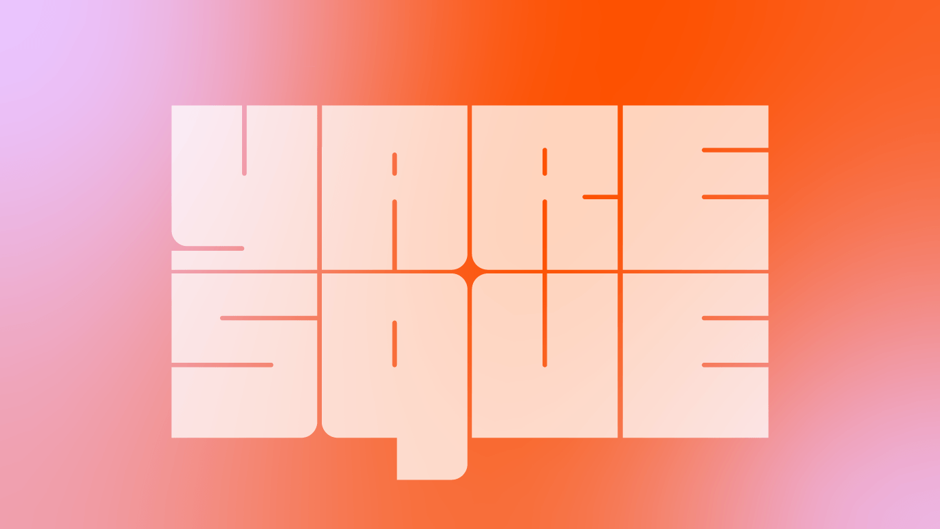 A person wearing headphones sits at a desk with a large curved monitor displaying graphic design software, surrounded by a laptop, smartphone, and potted plant, creating a modern workspace setup.