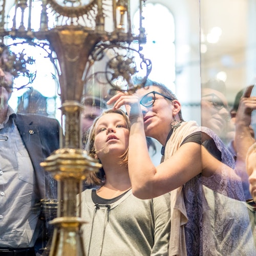 A group of people, including a child and an adult, closely observe an intricate ornate object behind glass in a museum.