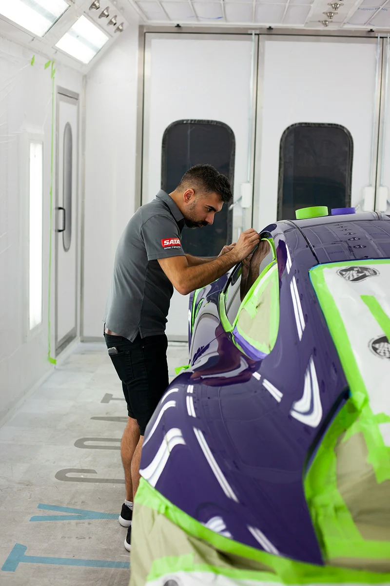 Professional technician installing paint protection film on a vehicle body panel in a detailing workshop.