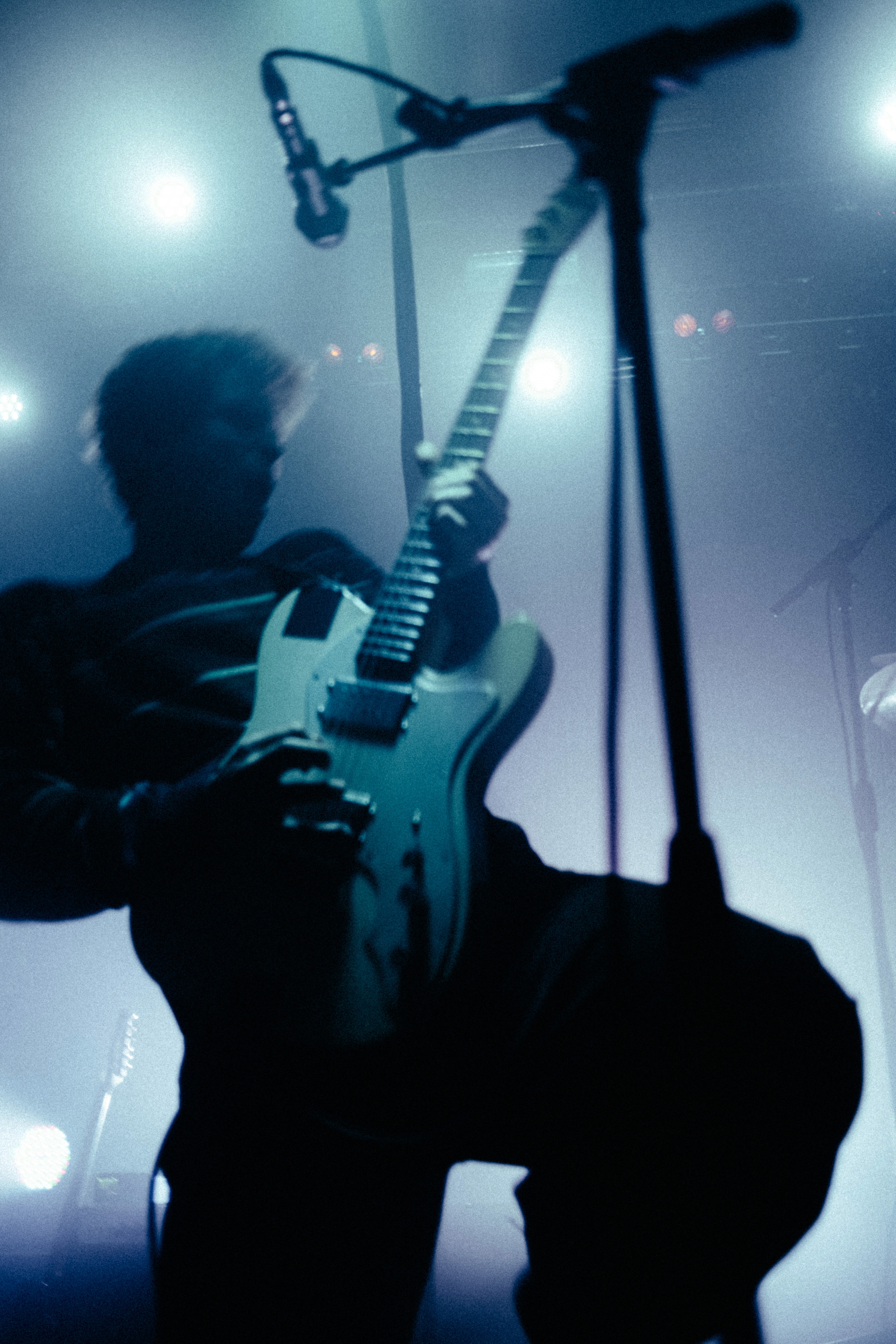 Silhouettenhafte Aufnahme eines Gitarristen auf der Bühne, der in dynamischer Pose sein E-Gitarren-Solo spielt. Blaue und violette Bühnenlichter erzeugen einen dramatischen Nebel und heben die Konturen des Instruments hervor.