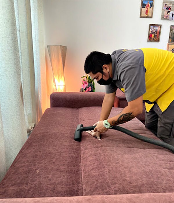 A man with a glove vacuuming a sofa with proper cleaning solutions for pet owners by Adams Care