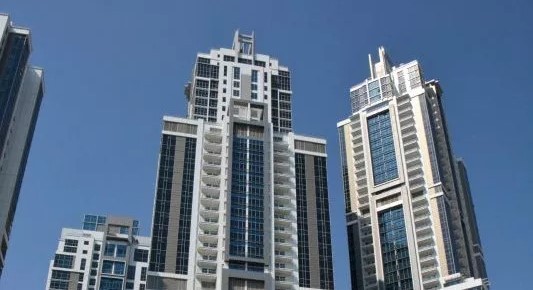 Direct low-angle shot up the facade of a tall Dubai office building, focusing on its window patterns.