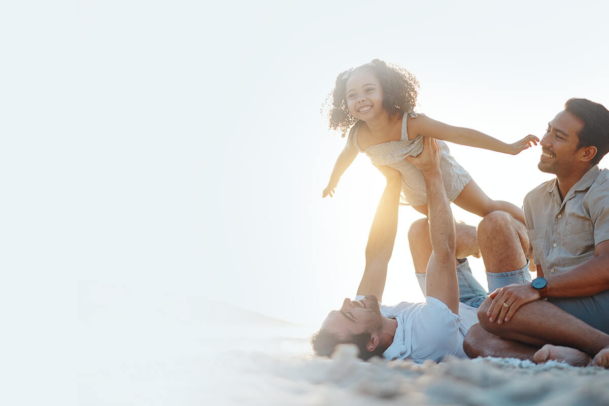 two dads playing with their daughter on the beach