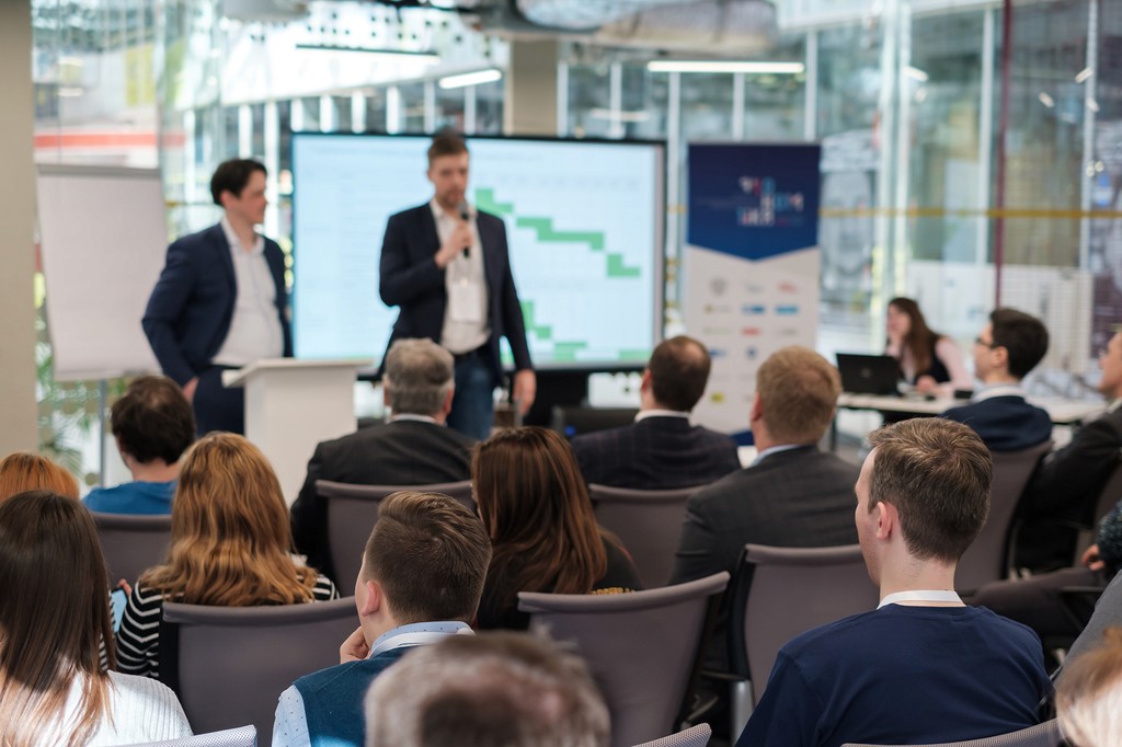 Dois homens de terno apresentando um plano organizacional para uma sala cheia de funcionários