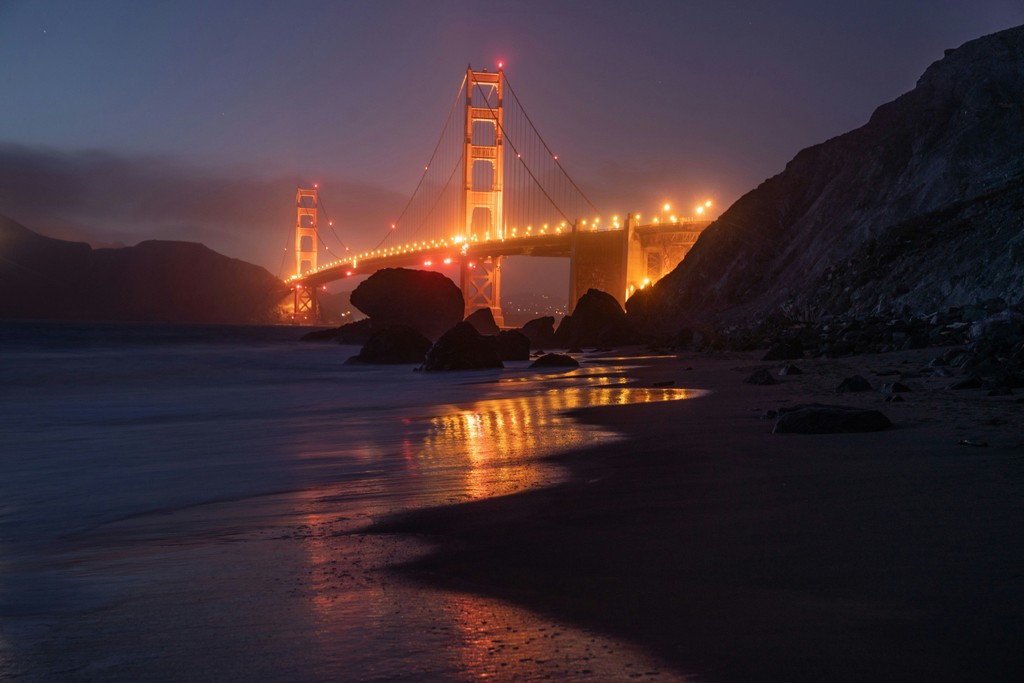 A beach at night with the Golden Gate Bridge glowing in the background