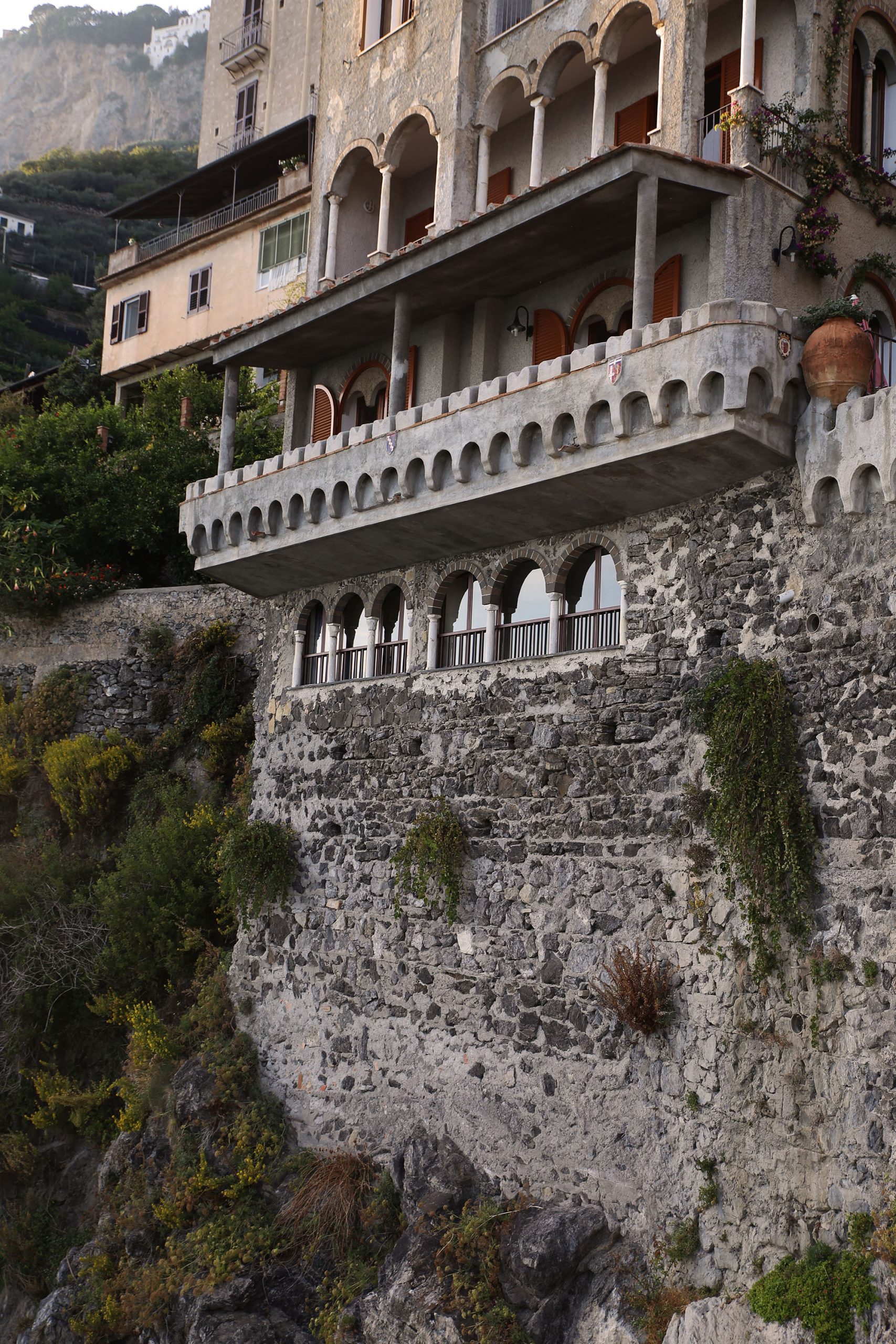 Castellated stone balcony with a coat of arms crest, built into a cliffside above the coast