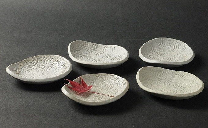 White pottery plates with Japanese designs etched in, adorned with a red maple leaf