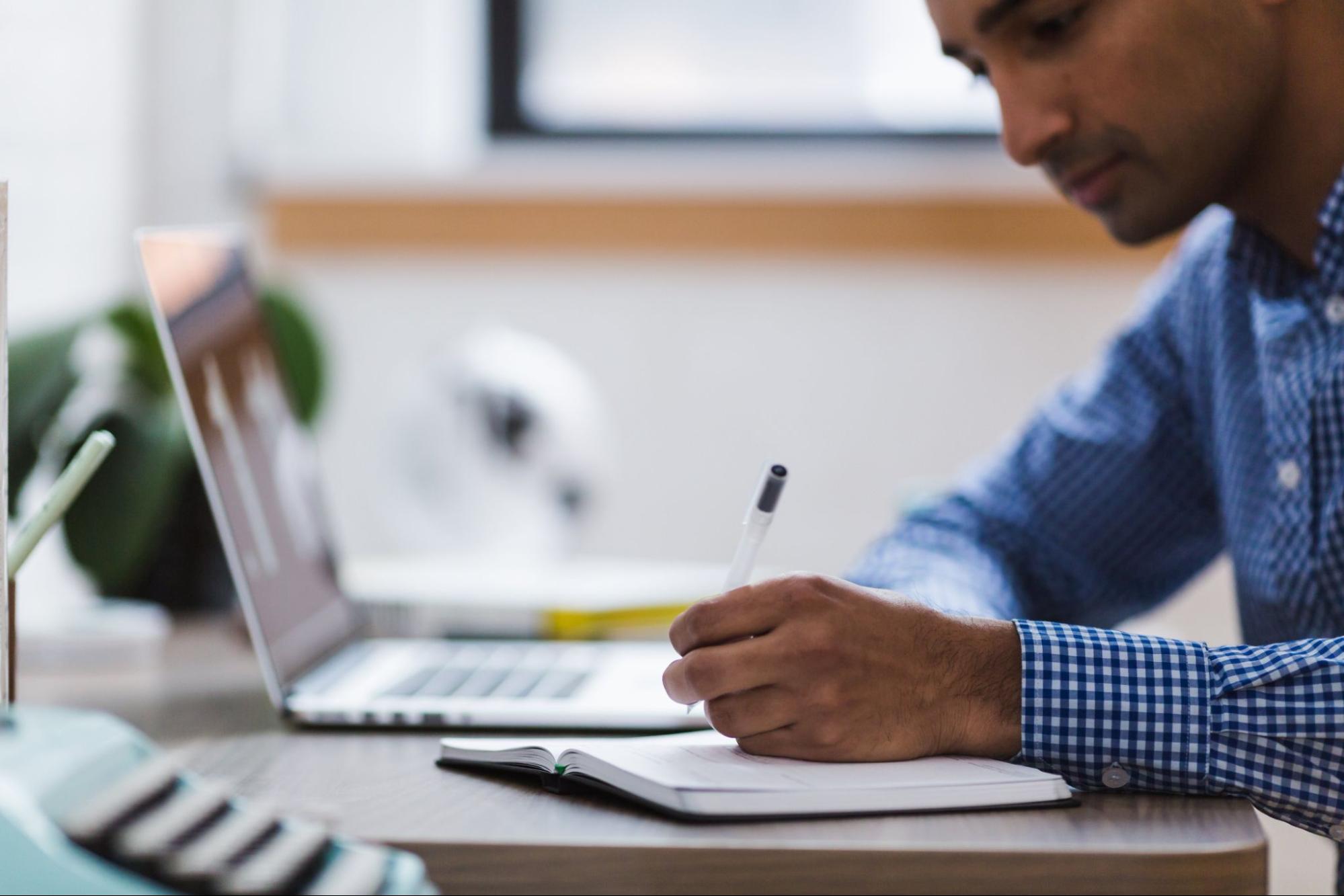 Researcher taking notes while reviewing interview findings on a laptop