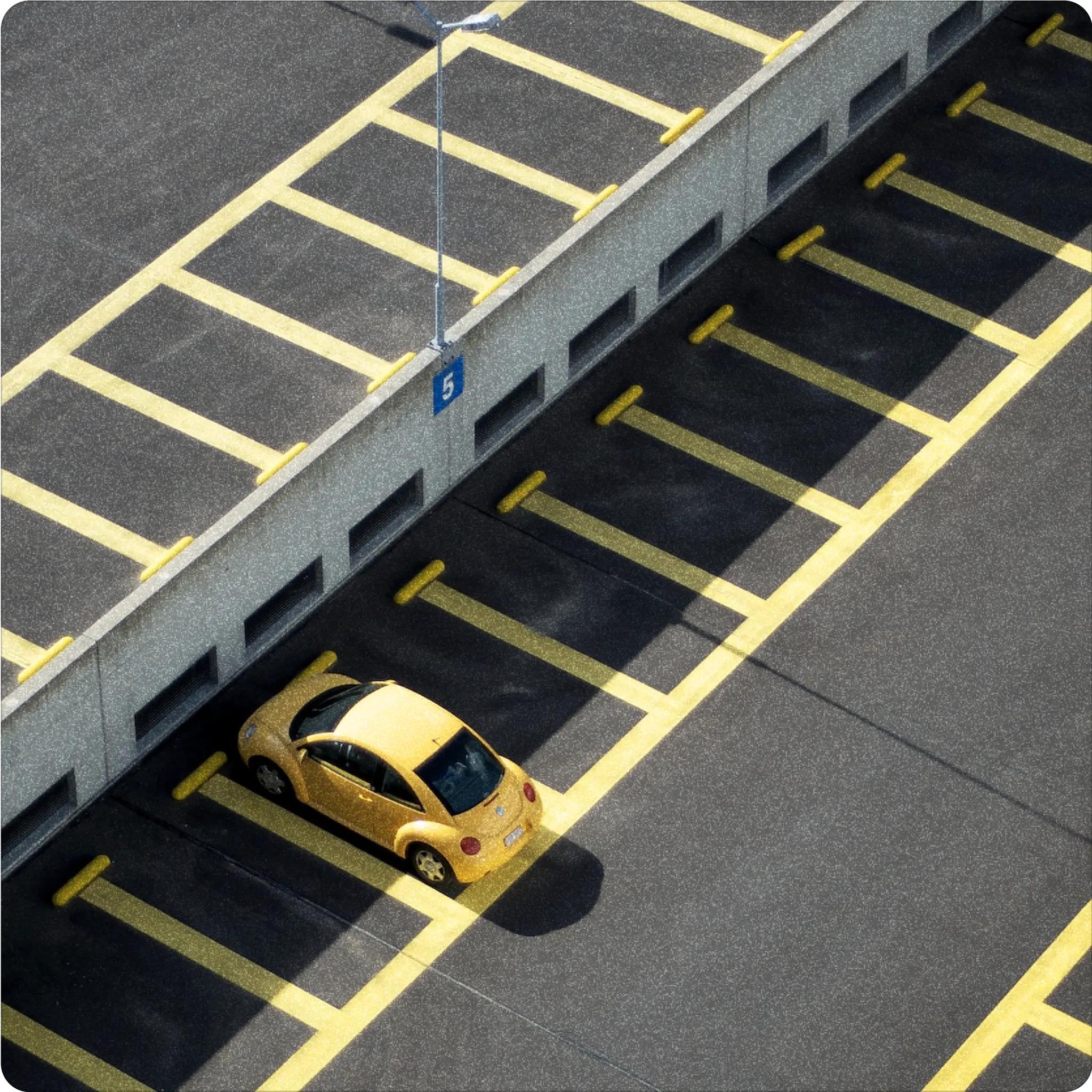 A yellow car parked in an empty parking garage, occupying one of the many available spaces marked by yellow lines.