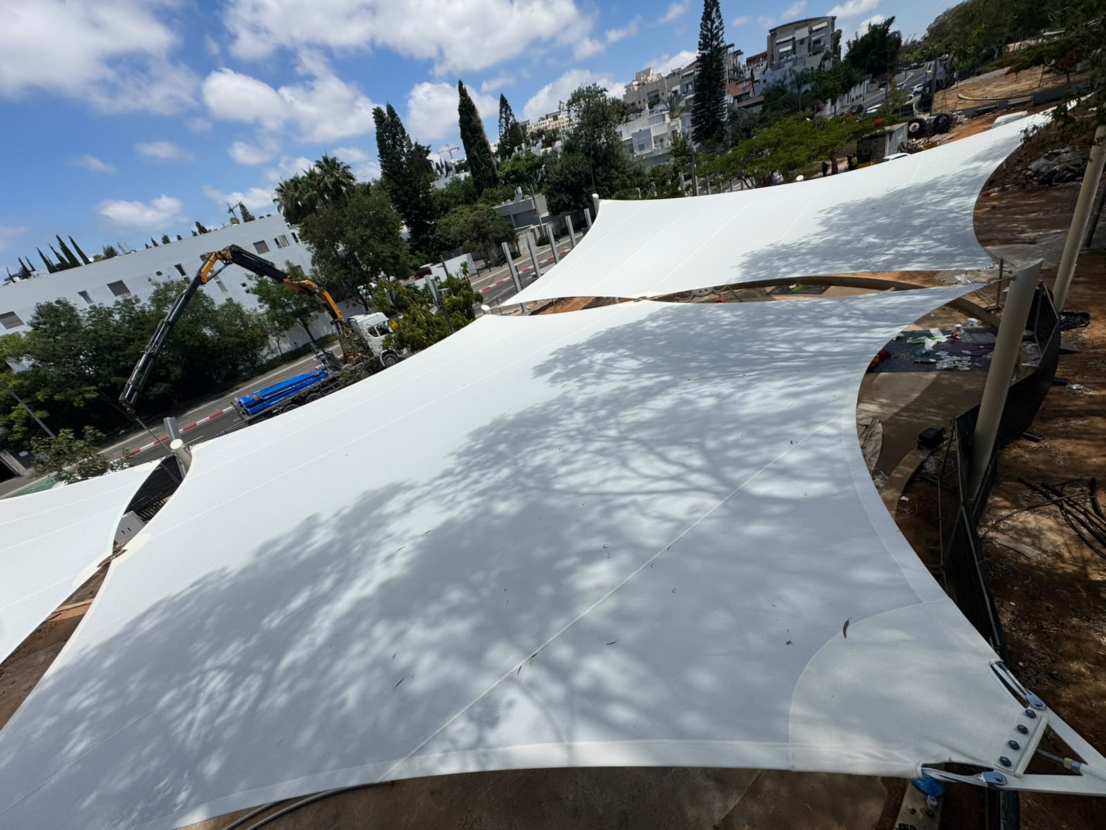 Large white sunshades over an outdoor area with trees and buildings in the background.