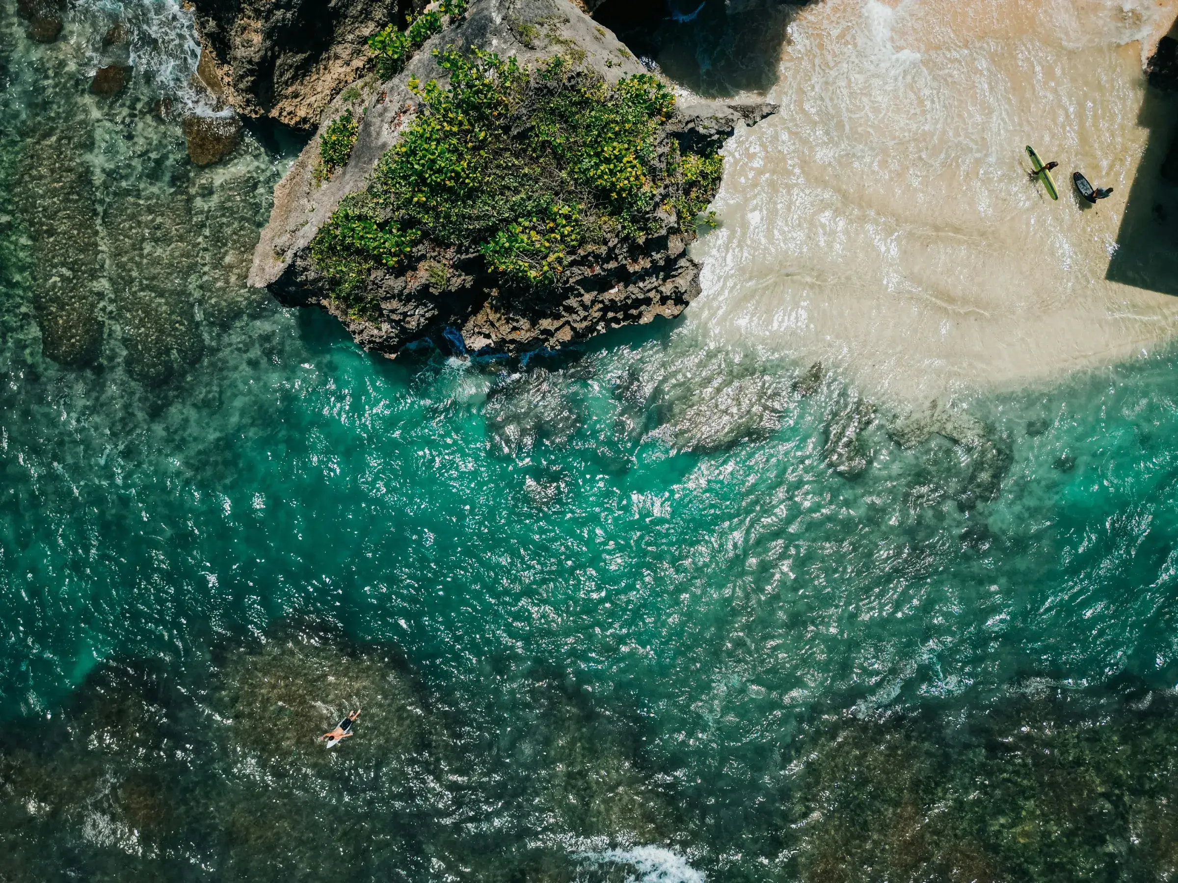 Aerial view of a stunning Bali beach and surfers, showcasing the tropical lifestyle of our multi-style yoga teacher training retreat