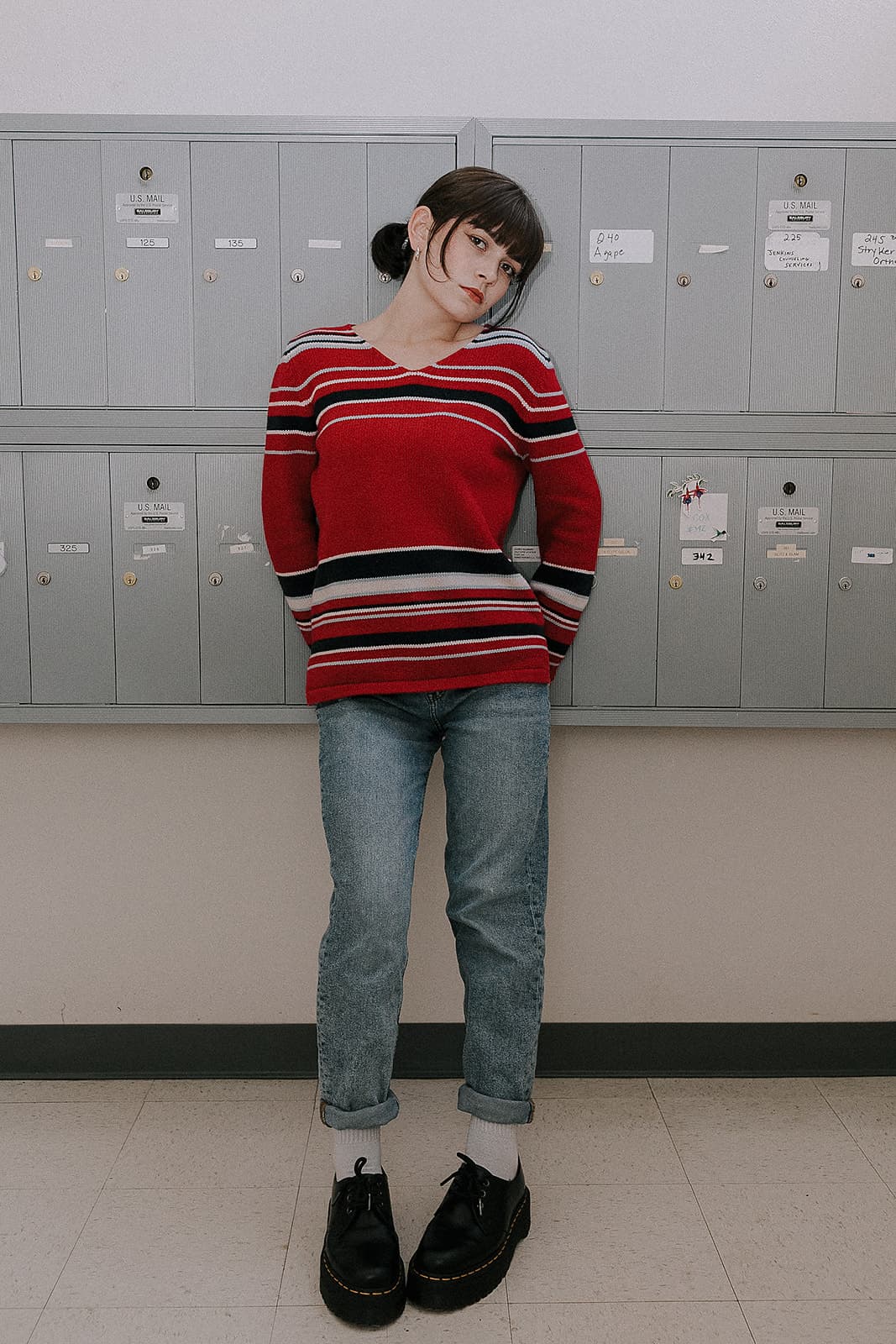 Model in striped red sweater poses casually against grey mailboxes at Revelator Studio’s natural light studio in Shreveport.