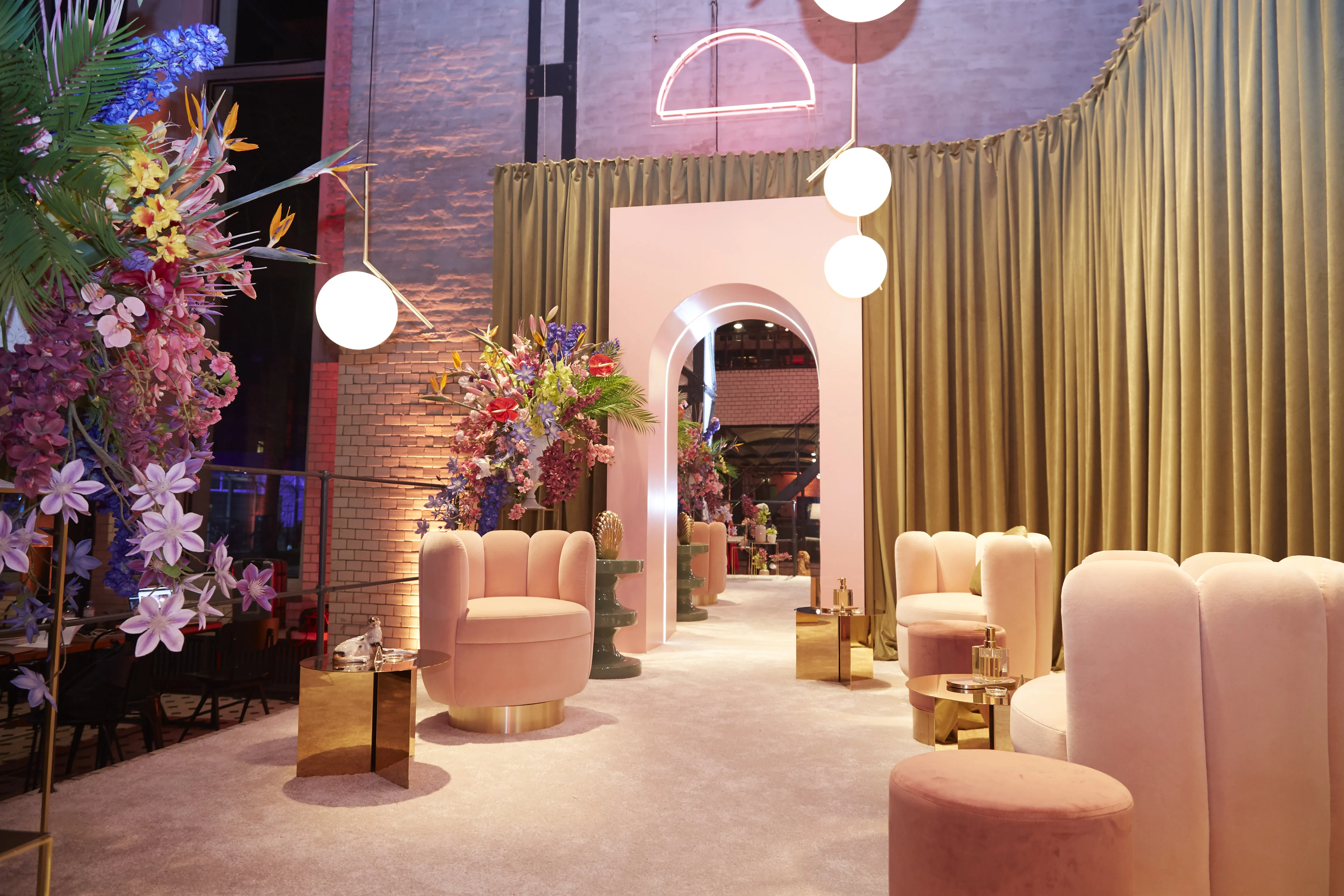 Rose-colored lounge area of the Klarna pop-up with curved velvet armchairs, gold side tables, arches and neon accents.