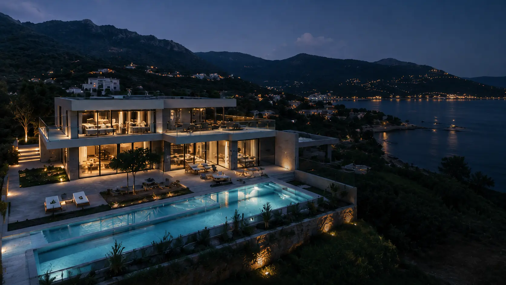 Vue drone d’une villa contemporaine en bord de mer au crépuscule, avec piscine à débordement illuminée et panorama côtier, réalisée pour le marketing immobilier.