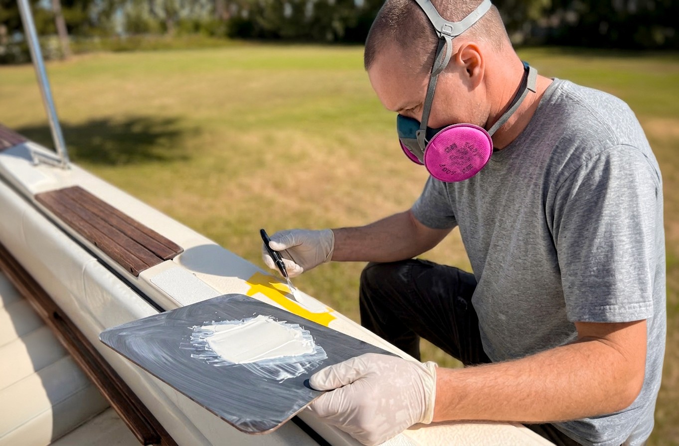 A man brushing gel coat onto the side of a boat