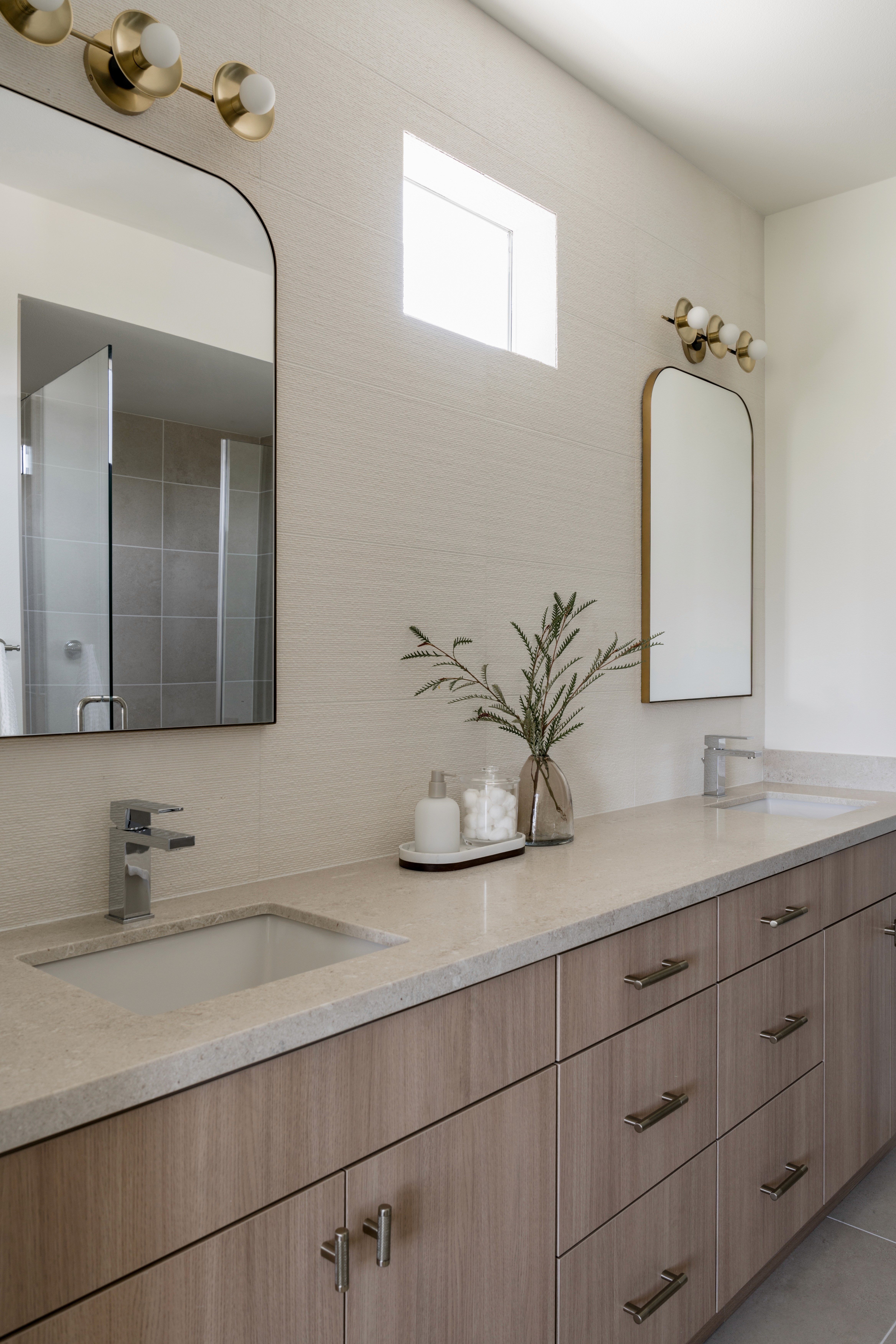 Dual sink vanity with light wood flat paneled cabinetry, off-white countertops, beige walls, rectangular wall mirror, and chrome faucet