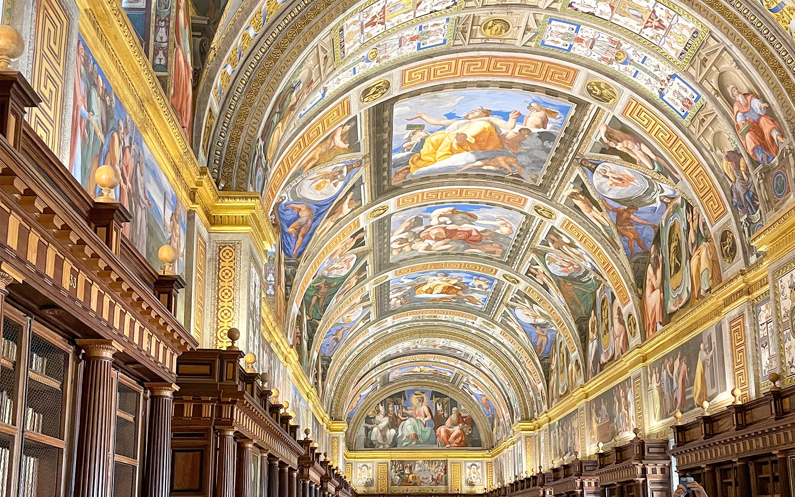 Loft bókasafnsins í El Escorial með nákvæmum freskum og skreyttum viðarbókahillum.