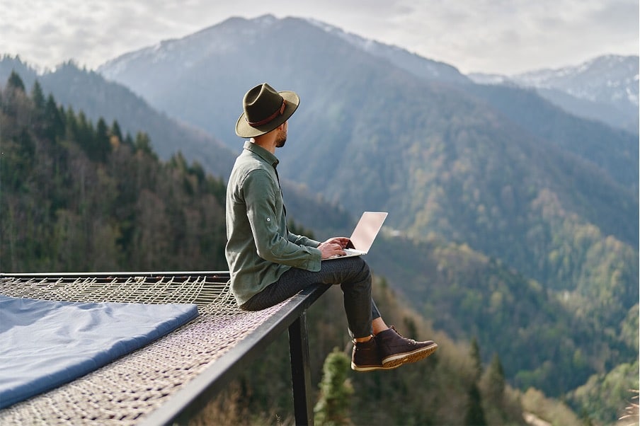 Man working on a laptop overlooking mountains in the background