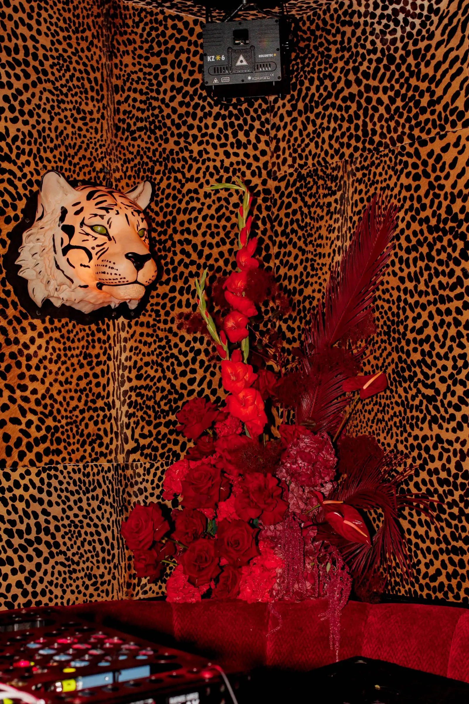 Rincón decorativo con flores rojas, pared de animal print de leopardo y una cabeza de tigre.