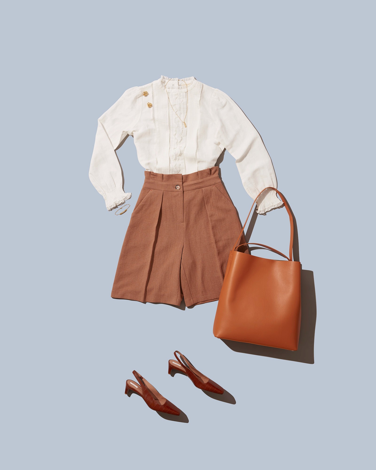Women's fashion outfit with white blouse, brown shorts, orange handbag, and matching slingback heels on blue background.
