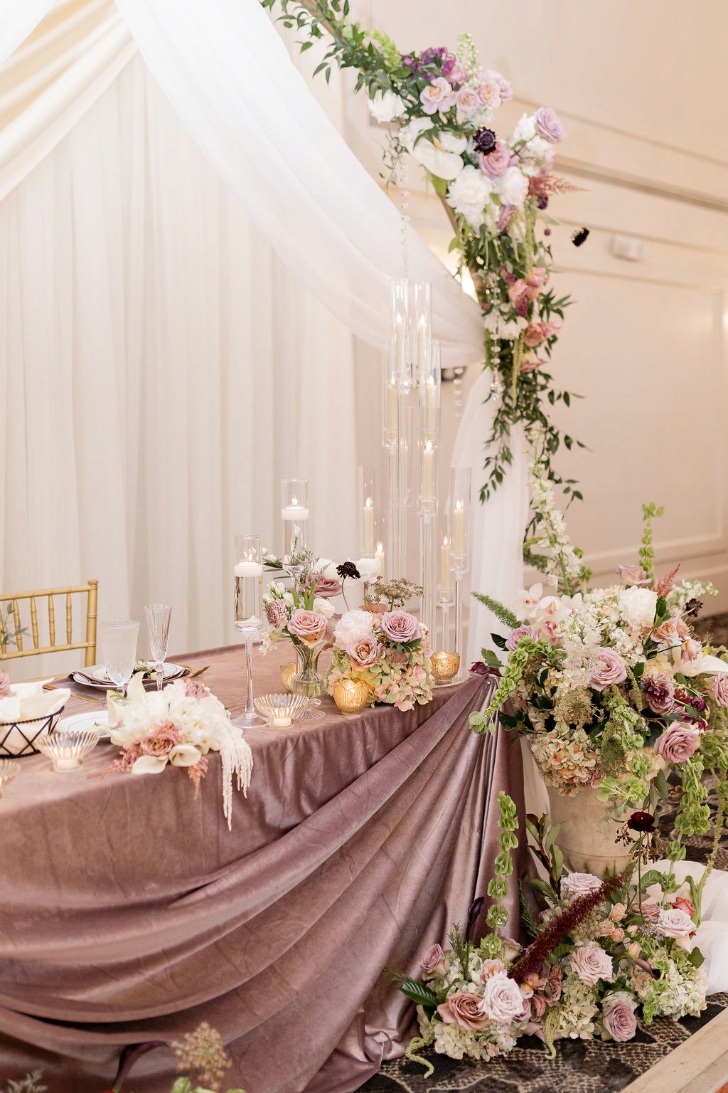 Pastel roses, tall glass candles and mauve draping decorate the reception sweetheart table.
