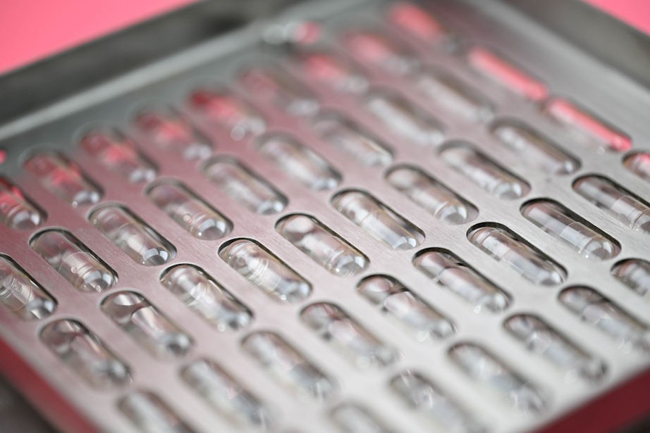 Close-up of neat rows of empty capsules in a metal compounding tray in a bright pharmacy lab setting