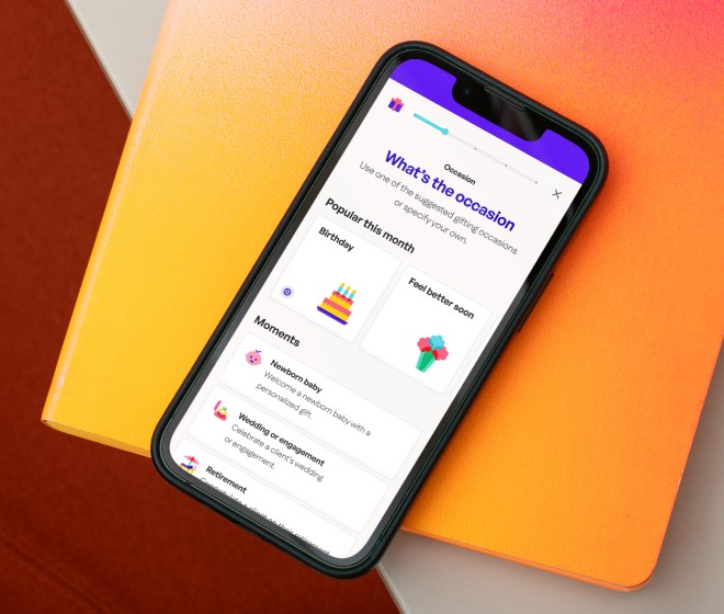 hanqs gifting app on a phone showing an occasion selector screen, resting on an orange notebook.